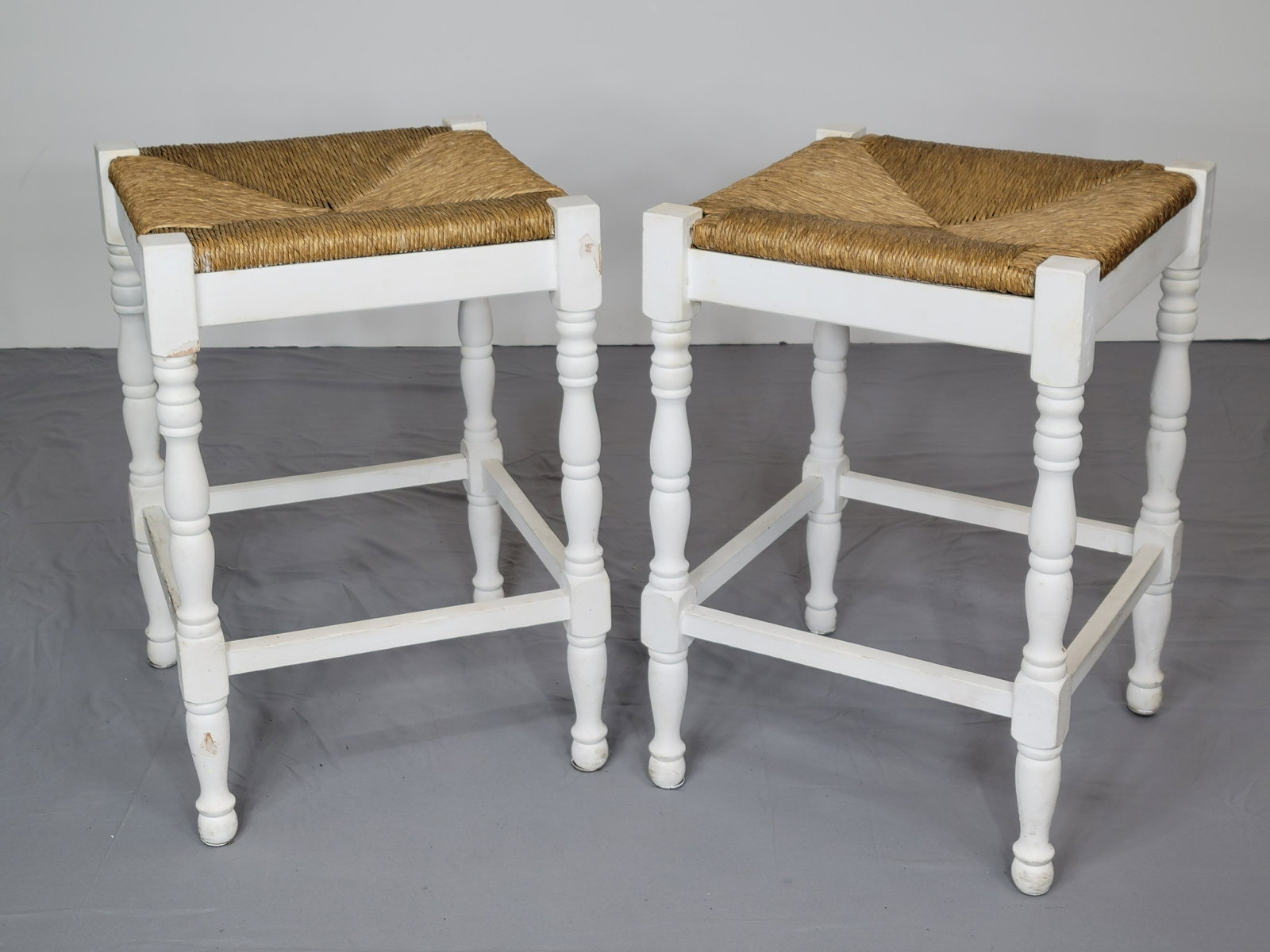 Pair Of Rush Seated Stools: 16 1/2" wide X 17" deep X 24 1/2" high. Has some discoloring and paint loss. MG. IMPORTANT: Before bidding, please read the terms and conditions. When you registered for the auction you agreed to thes