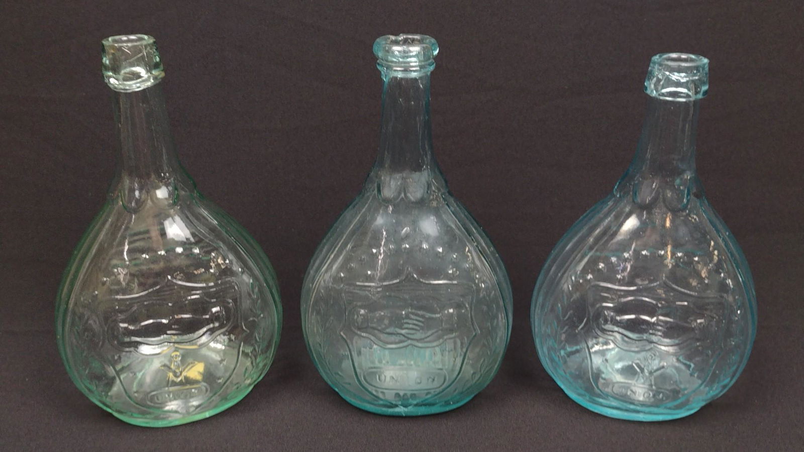 3 Union Shield Flasks incl Blown: Each 5" wide X 8-3/4" to 9" high. DM IMPORTANT: Before bidding, please read the terms and conditions. When you registered for the auction you agreed to these terms and will be required to comply with