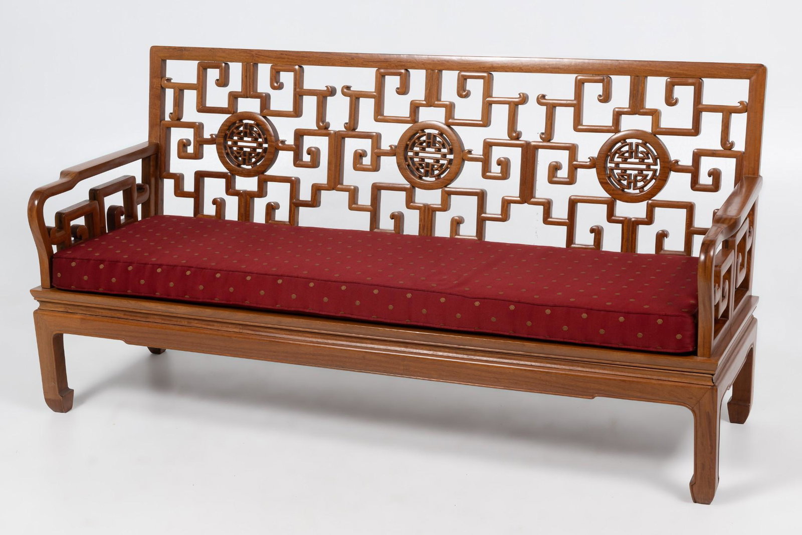 Chinese Carved Rosewood Sofa: Chinese carved rosewood sofa. Three carved medallions along back of sofa with angular spirals emanating from the medallions. Red with tan polka dot cushion. 33" high x 21" deep x 65" wide. Missing cen