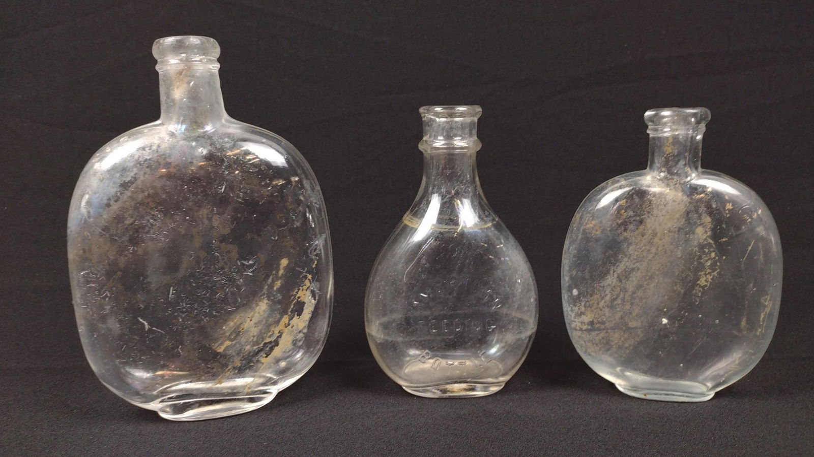 3 Antique Flasks and Bottles: Includes American Feeding Co. 3-1/2" to 4-1/2" wide X 5-1/4" to 6-3/4" high. One with loss to mouth. DM IMPORTANT: Before bidding, please read the terms and conditions. When you registered for the auc