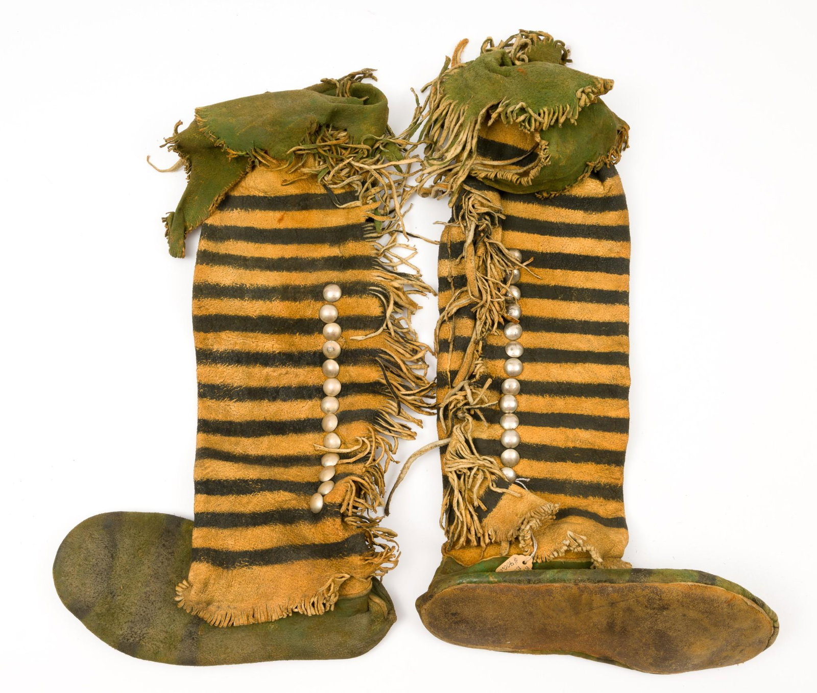 Pair of Plains Indian Dance Boots: Pair of dyed and brass decorated Plains Indian dance boots. 20th century. Stated to be Kiowa in origin. Hide shin length boots with polychrome blocks and applied brass studs.10-1/2" long x 4" wide x 1