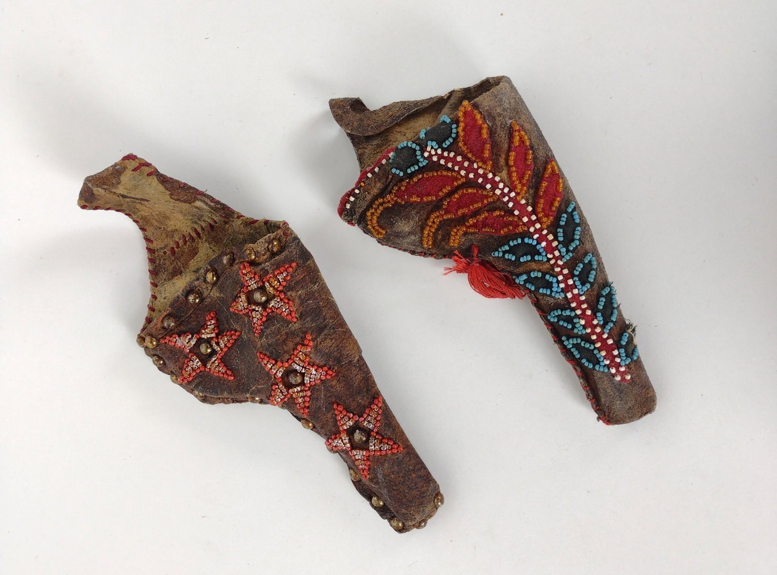 2 Western Style Beaded Holsters: Late 20th century aged holsters. Intended to hold Colt Army revolvers. One with beaded stars, the other with plant/leaf design with attached tassel. 6-1/2" long x 4" wide and 8-3/4" long x 4" wide. RM