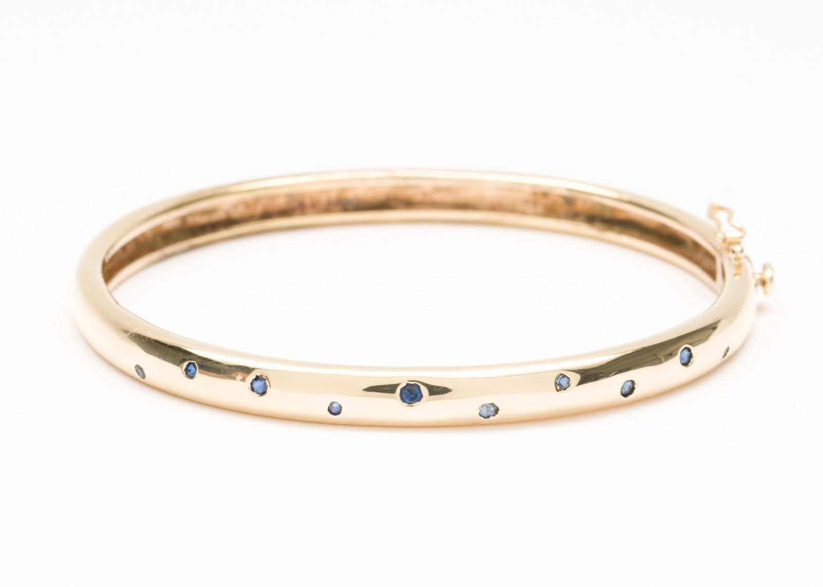 Bailey, Banks & Biddle 14K Gold & Sapphire Bangle: DESCRIPTION: 14k (stamped) gold bangle bracelet flush mounted to top section with ten round cut blue sapphires. Also stamped for maker with lower case "m" in circle. Includes Bailey, Banks & Biddle br