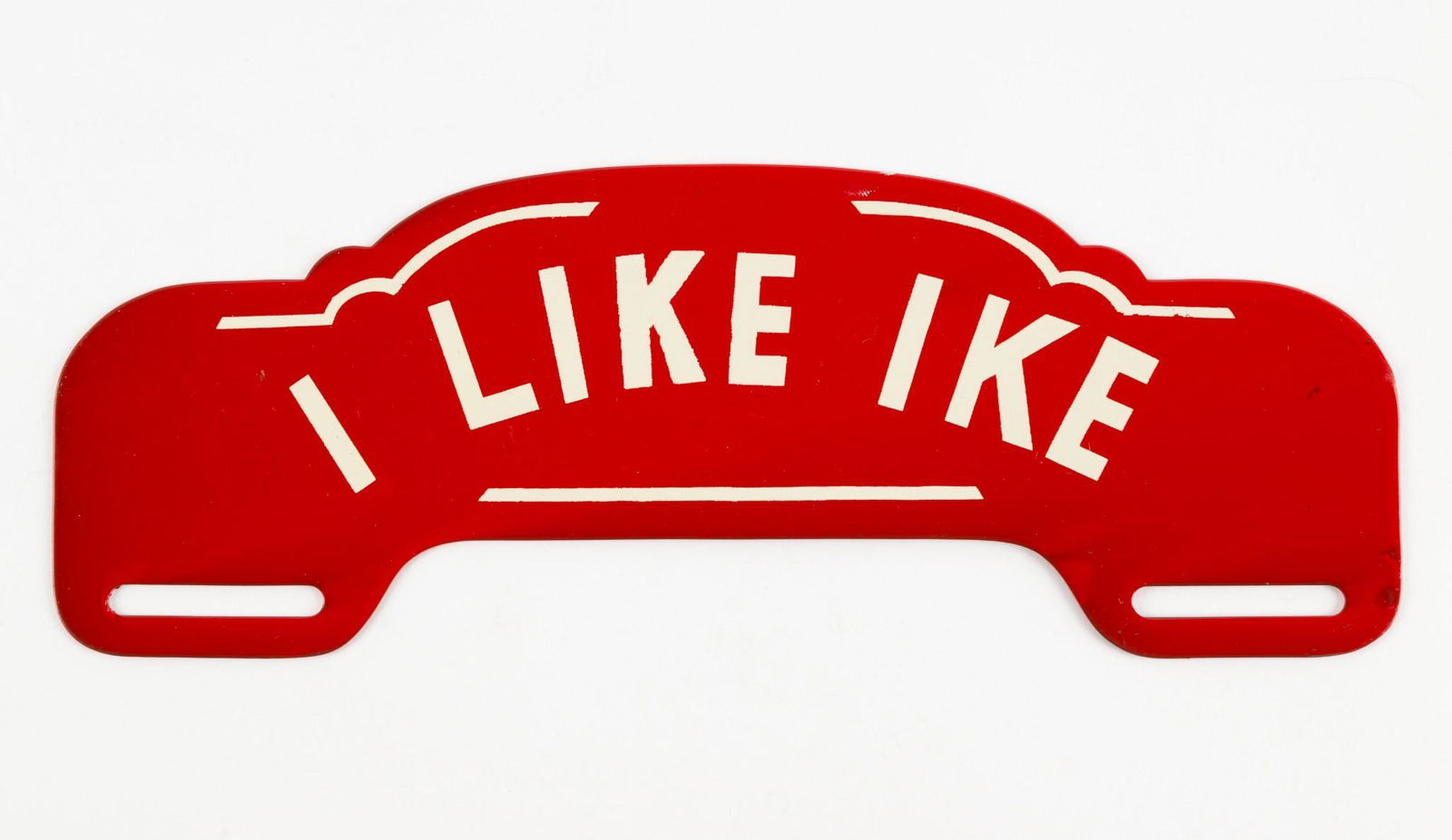 1952 "I Like Ike" License Plate Topper: Red embossed metal license plate topper with red lettering "I Like Ike". Excellent condition. 3-1/2" high x 10" wide. Small dings and black marks to right edge. Small marks throughout. DP. IMPORTANT: