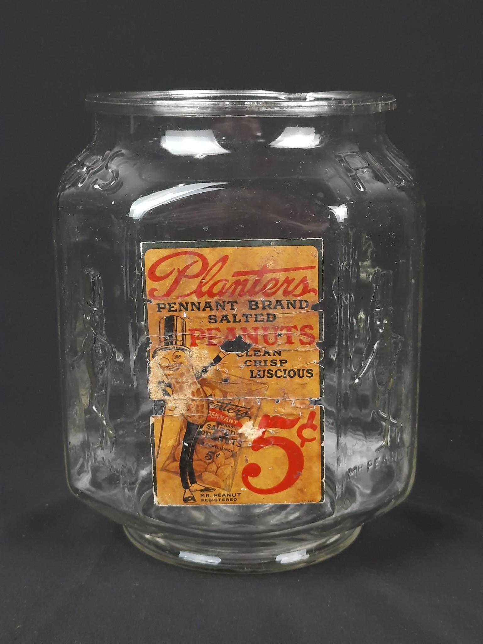 Planters Peanut Jar: 8" wide x 8" deep x 10-1/2" high. Some losses to paper liable. Loss to top jar rim. LR IMPORTANT: Before bidding, please read the terms and conditions. When you registered for the auction you agreed t