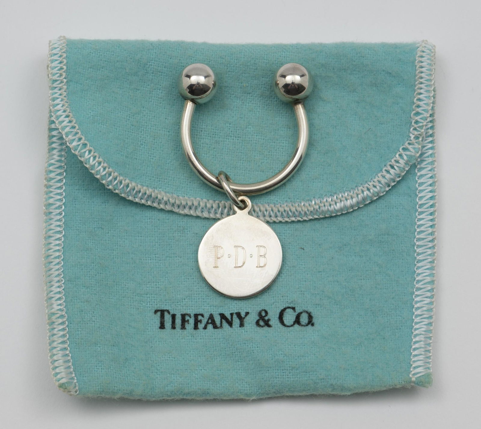 Monogrammed Sterling Tiffany & Co. Keychain: Keychain with sterling monogrammed charm. Marked Tiffany & Co. to back. Includes dust bag. Charm 1" long. Ring 1-1/8" long x 1-1/8" wide. 0.3 ozt. Light surface scratches as expected with careful use.