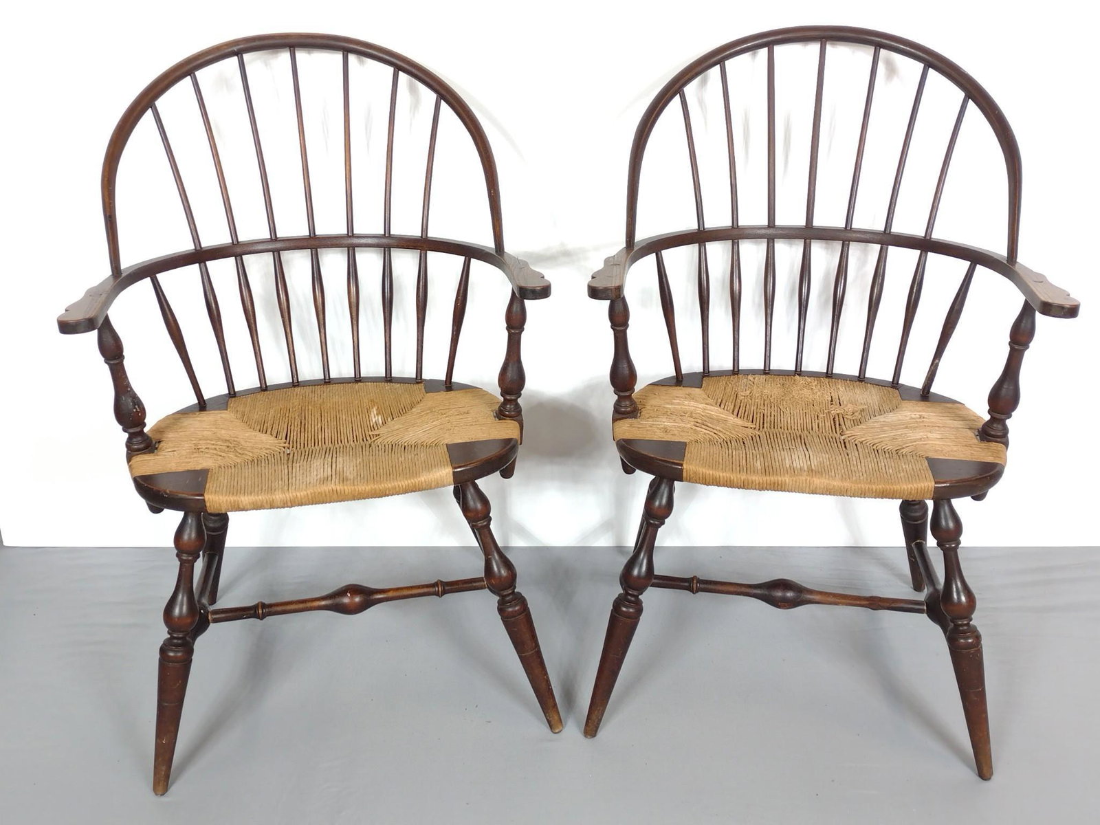 Pair Of Rush Seat Windsor Arm Chairs: Each 24-1/4" wide X 16" deep X 37-1/2" high. Both have scratches. One has repaired spoke. MG. Provenance: From the estate of Mary Trost who last resided in the multi generational family home located i