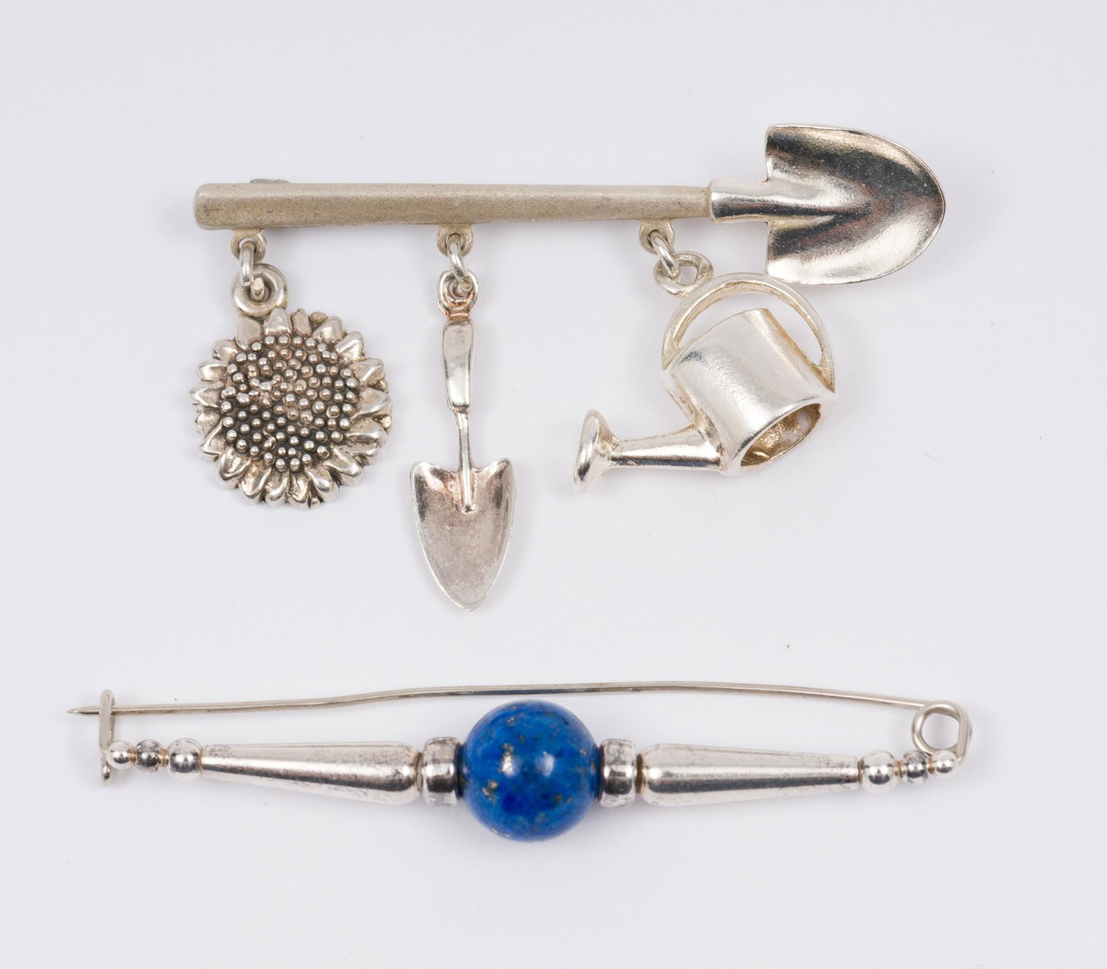 2 Silver Pins Incl Charm: Includes one shovel pin with 3 charms: trowel, watering can, and sunflower, stamped 92.5. Other pin with lapis bead, unmarked. 2-3/8" to 2-7/8" long. AJ/EK IMPORTANT: Before bidding, please read the t