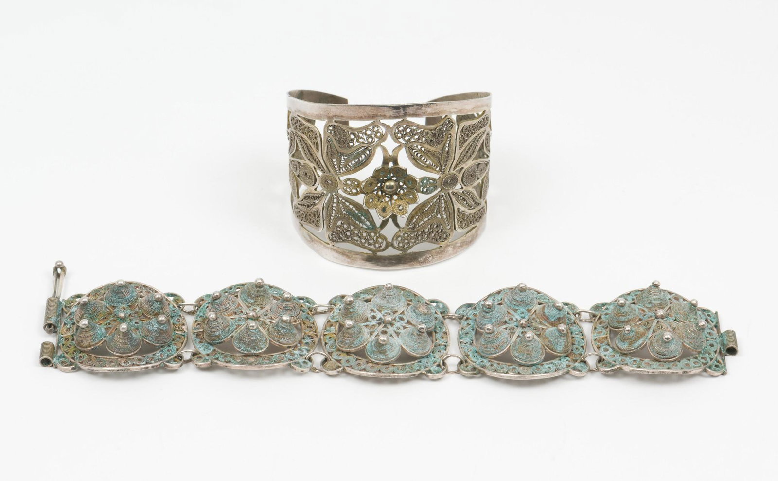 2 Bracelets: Includes one floral design and one with circular design with six raised cones inside. Both with 2" diameter. 1-1/4 and 1-3/4" wide. Some corrosion and wear. One cone is missing the top bead. No marks.