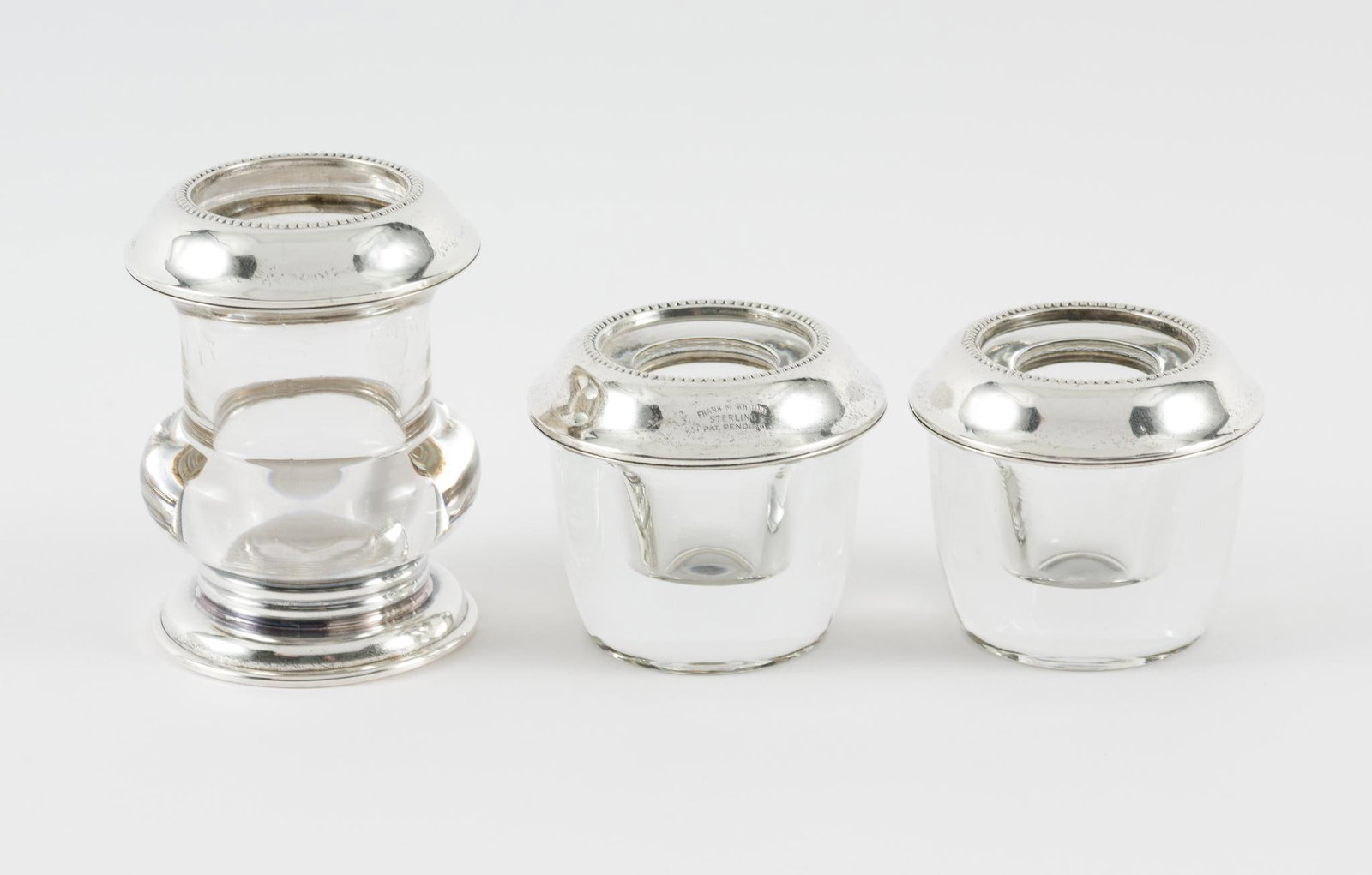 3 Frank M. Whiting Glass & Sterling Holders: One cigarette and two lighter holders. Marked Frank M. Whiting & ; Sterling. 2-1/4" diameters and 2" and 3" high. Light scratches and wear as expected with age and use. AJ.
