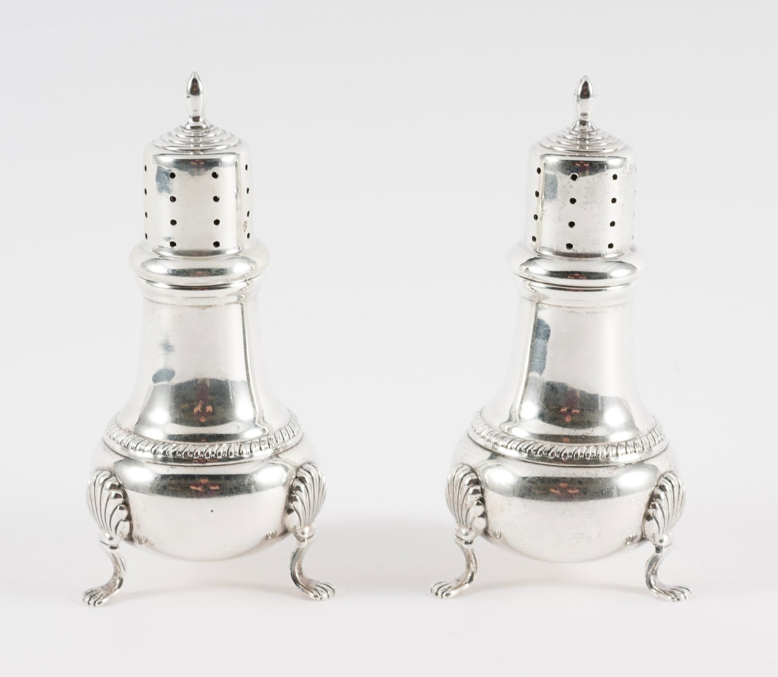 2 Sterling Salt & Pepper Shakers: 2 salt and pepper shakers with removable tops and 3 legs. Marked "K H" and sterling to bottoms. 2" wide x 4-1/2" high. 5.2 total ozt. Light scratching and wear as expected with age and use. AJ.