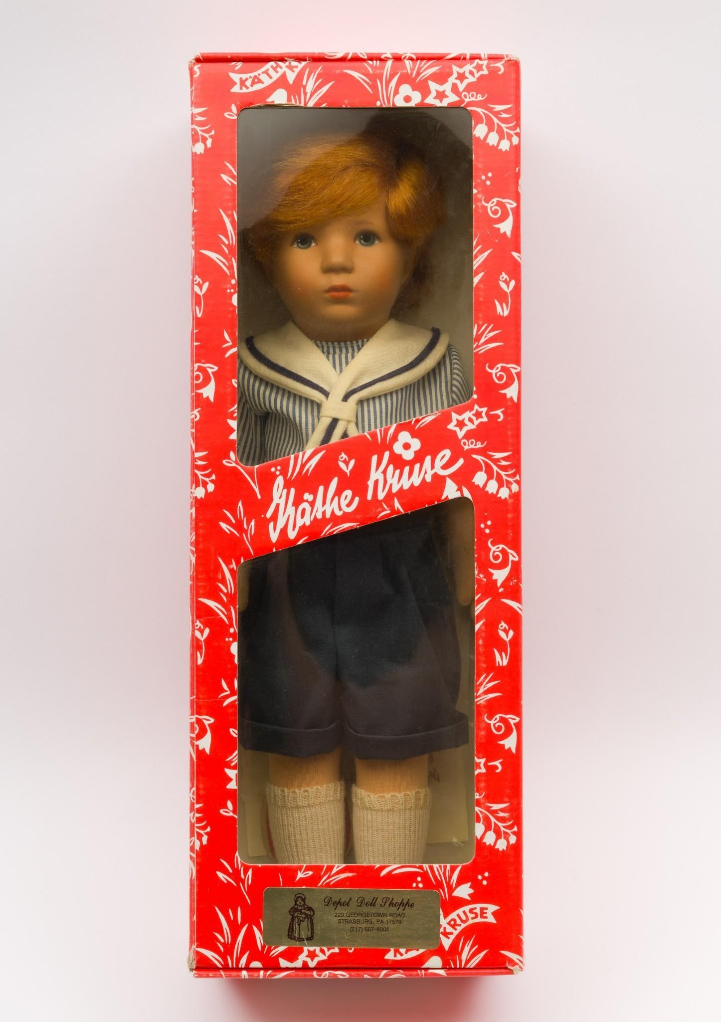 Kathe Kruse Doll: Kathe Kruse model Hanne Kruse. In original box with pamphlet. Resin face with cloth body, arms, and legs. Strawberry blonde hair wearing a blue striped shirt, blue shorts, white socks, blue buckle sho