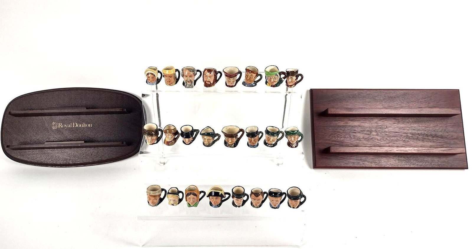 24 Miniature Royal Doulton Mugs: Each approx. 1" high. Also includes 2 wood display stands.