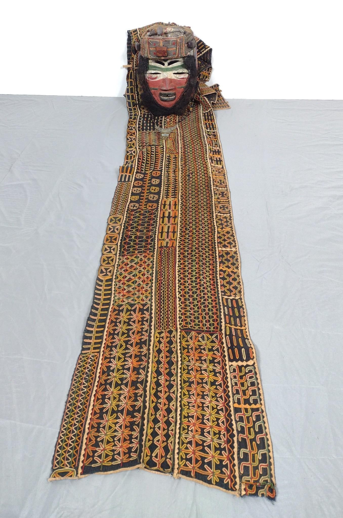 African Tribal Mask Displayed with Tunic and Necklace: Mask 12” high x 8” wide. Overall 64" long. PROVENANCE: From the Estate of James L. Stanfield, Veteran National Geographic photographer (1937-2023). Mr. Stanfield was one of the world's mos