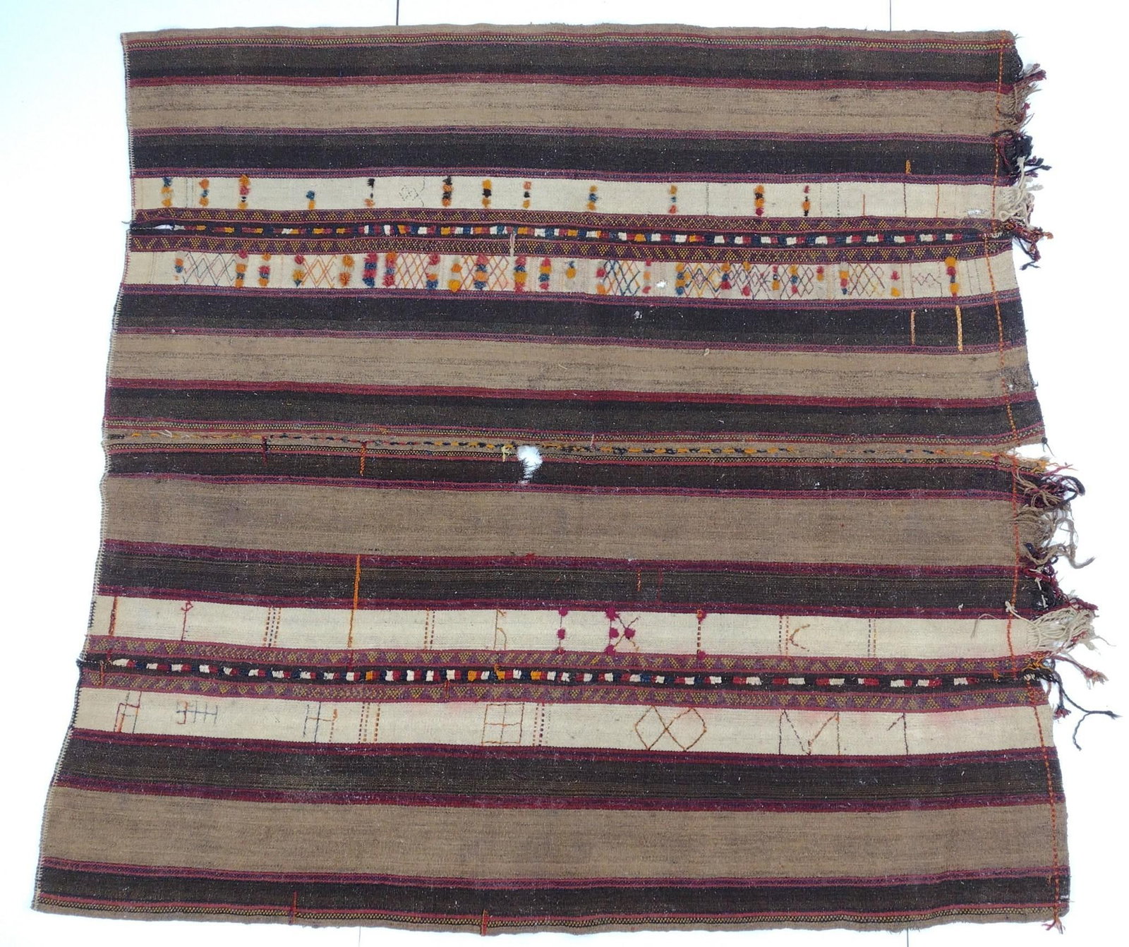 Tribal Area Rug: NOT ELIGIBLE FOR IN-HOUSE SHIPPING. 7'7" long X 6'11" wide. Has some holes and edge damage. PROVENANCE: From the Estate of James L. Stanfield, Veteran National Geographic photographer (1937-2023). Mr.