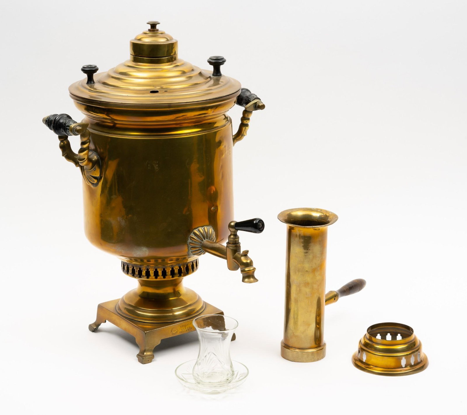 Russian Samovar with Funnel and Cup with Saucer: Mark to left of spout not complete. Samovar: 12-1/2" wide x 13-1/2" deep x 18" high. Funnel: 8-1/2" wide (to end of wood handle) x 8" high. Glass cup with saucer: Overall 4" diameter x 3-1/2" high. Al