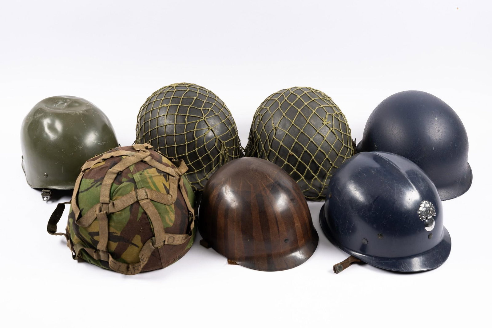 6 Military Helmets: Includes U.S. M1 helmet liner; French F1 helmet; Belgian riot helmet; (2) Austrian 1976 Army helmets and covers; and Belgian military helmet. All with wear to them.
