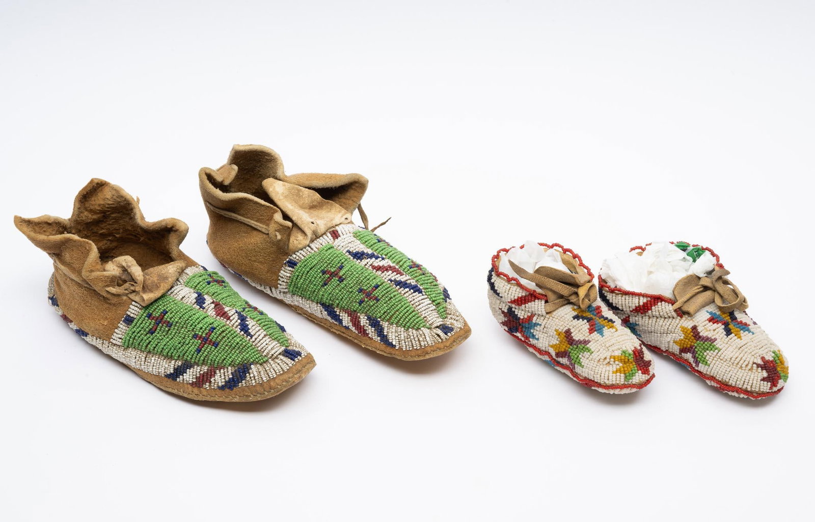 Cheyenne Children's Fully Beaded Moccasins And Lakota Sioux Adult Moccasins: A superb fully beaded pair of Cheyenne toddler or baby moccasins. White ground with multicolored stars. Probably early to mid 20th century. These fully beaded children's moccasins have work that exten