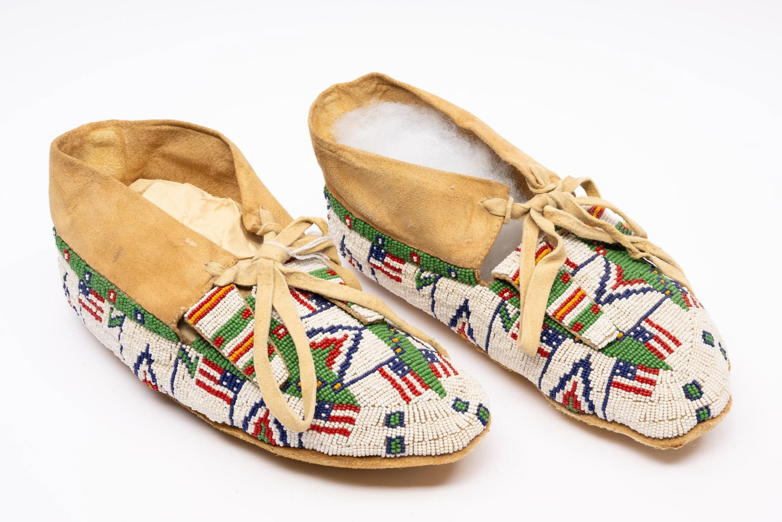 Pair of Sioux Flag Motif Moccasins: A lovely pair of Lakota Sioux beaded moccasins probably second half of the 20th century. White ground with green, red, and blue geometrics and American flags. Flag motif Sioux items are among the most