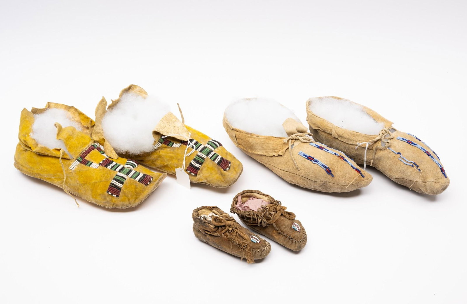 3 Pairs Southern Plains Indian Moccasins: Three pairs of Southern Plains Indian moccasins. Two showing evidence of wear and light use. All made from light tanned hide to which are attached simple geometric beaded strips. Two adult pairs and t
