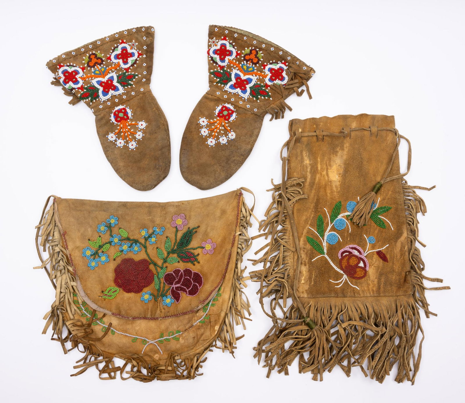 4 Cree Beaded Items: Two Cree bags and a pair of mittens with beaded floral work on tanned hide. Probably early 20th century. Measurements: Mittens - 12" Satchel - 12x12" Bag - 15-1/2" Condition: Overall good.