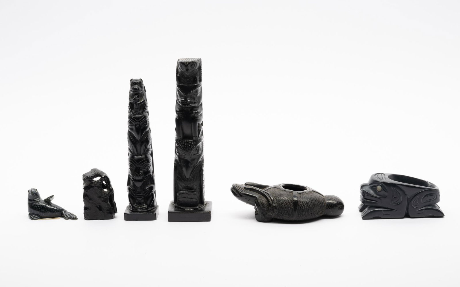 Six Argillite Pacific Northwest Carved Objects: A group of six different carved argillite Pacific Northwest Tribal carvings made for the tourist market. 20th century. Measurements: 1-1/4" to 6". Condition: Overall good.