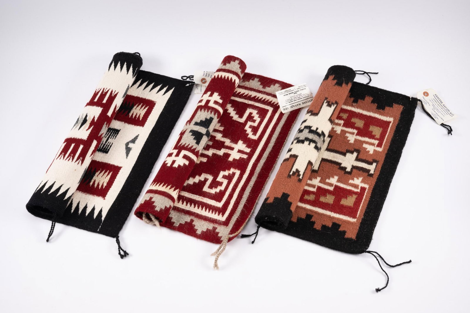 3 Navajo Ganado Mats: Three late 20th century Ganado mats with old tags from Pfoutz Trading Room identifying the weavers as follows: Red Rug Tag: name unreadable Tan Rug Tag: Mary J. Begay White Rug Tag: Elsie Whitehorse M