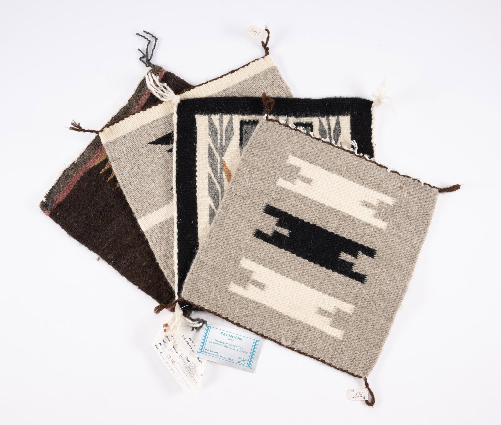 4 Navajo Weavings: A group of four small square Navajo mats. The dark bordered Yei has a Pfoutz label noting that it was made by Bessie Begay.. The Dark Eye-dazzler has a note that it was made by Pat Moone, The other tw