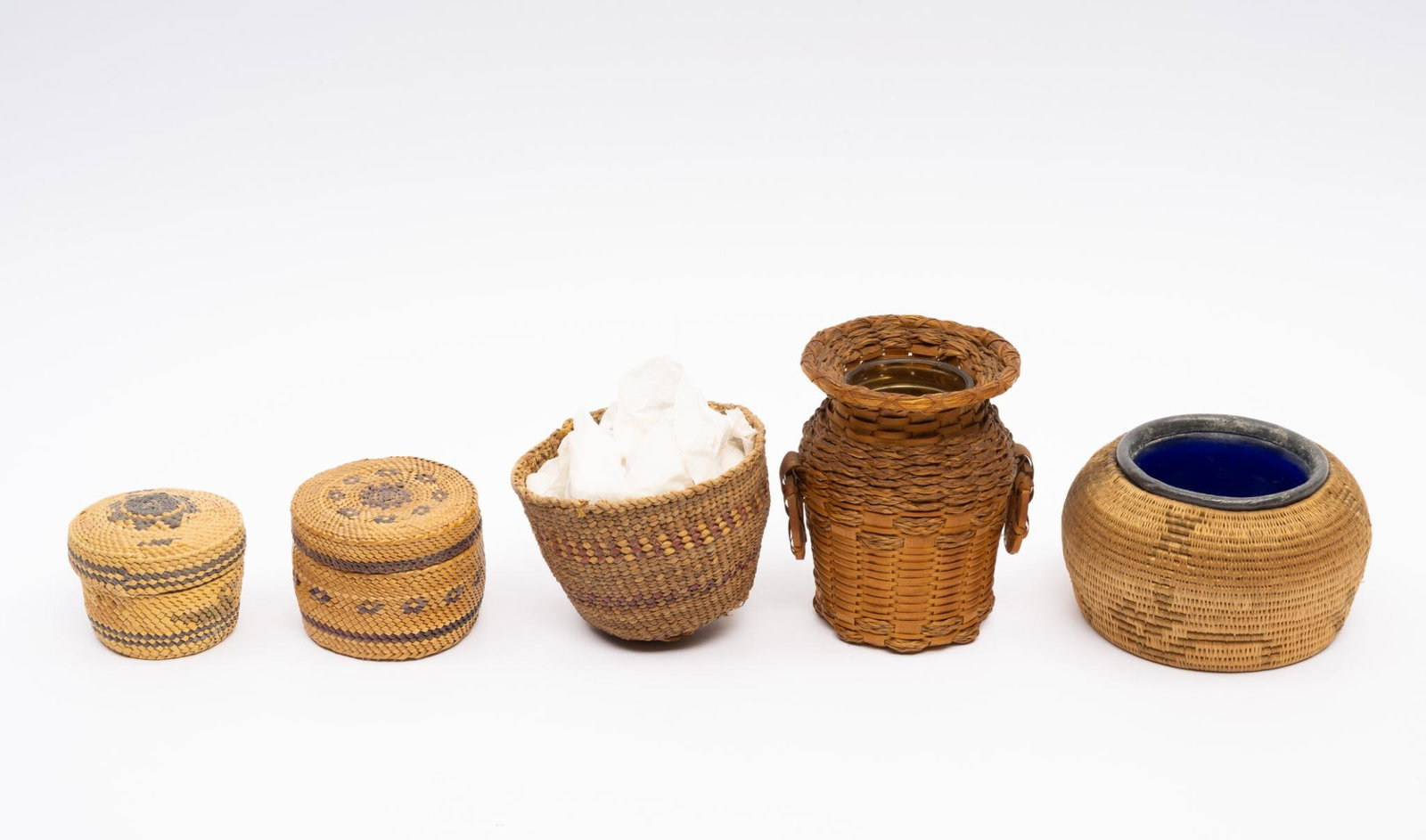 5 Miniature Baskets: A group of five miniature baskets produced by Pacific Northwest and Eastern Woodland tribes. One a cover for a cobalt blue inkwell liner. All late 19th or early 20th centuries. Measurements: 2" to 4".