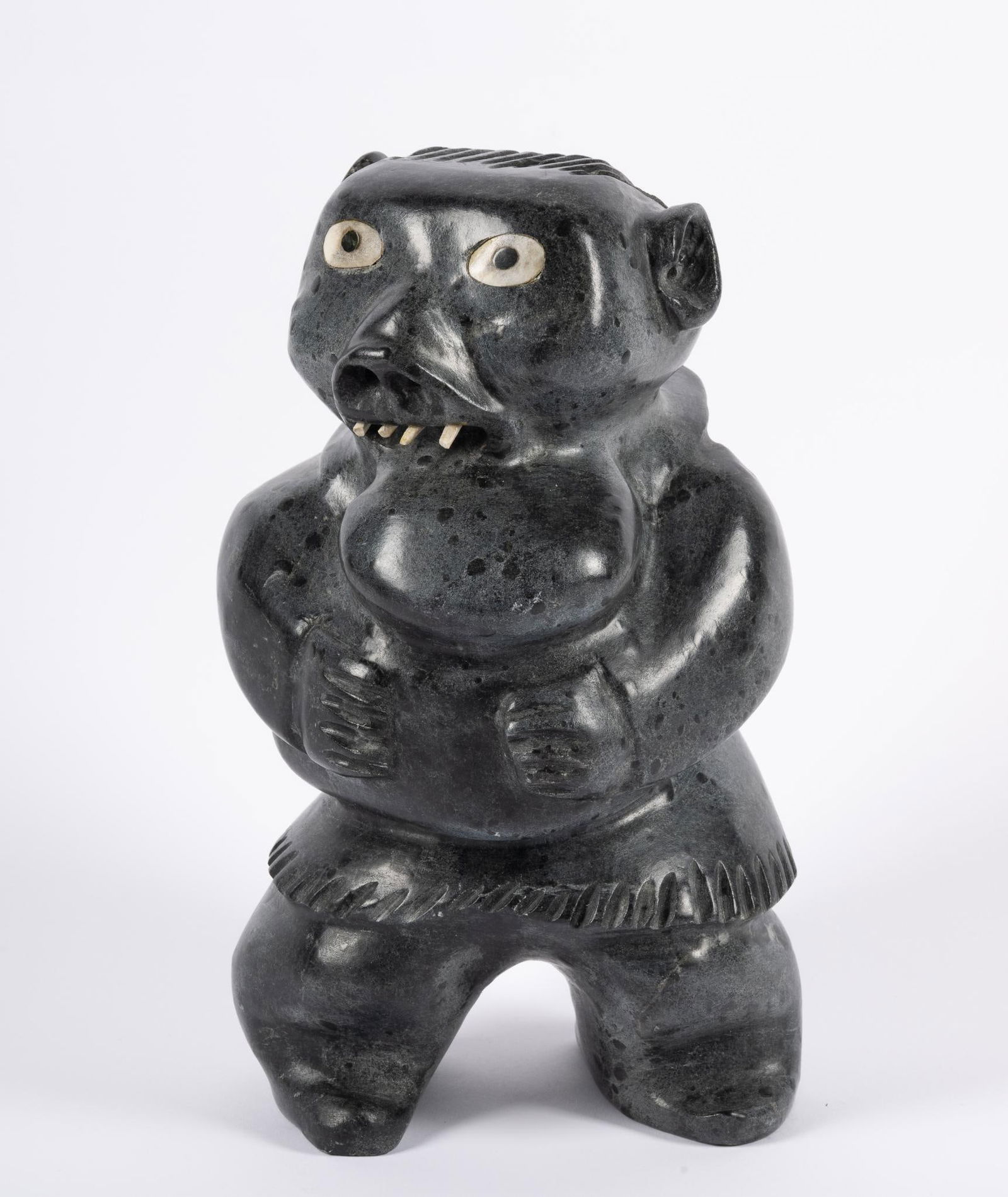 Inuit Carved Stone by Judas Ullulaq: NOT ELIGIBLE FOR IN-HOUSE SHIPPING Dark soapstone figure of a shaman eating bread. Judas Ullulaq (Inuit, 1937 - 1999) was a celebrated artist, recognized for his figural and zoomorphic sculptures. His