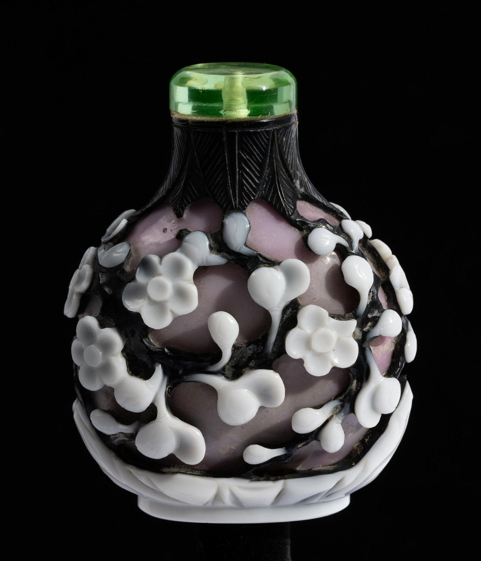 Chinese Double Overlay Carved Peking Glass Snuff Bottle: DESCRIPTION: White flowers on vines decorate a purple glass snuff bottle. Lid is clear green glass. MEASUREMENT: 2-1/2" wide x 3" high, 3 1/4" height with stopper. CONDITION: Lid is glued in place (st