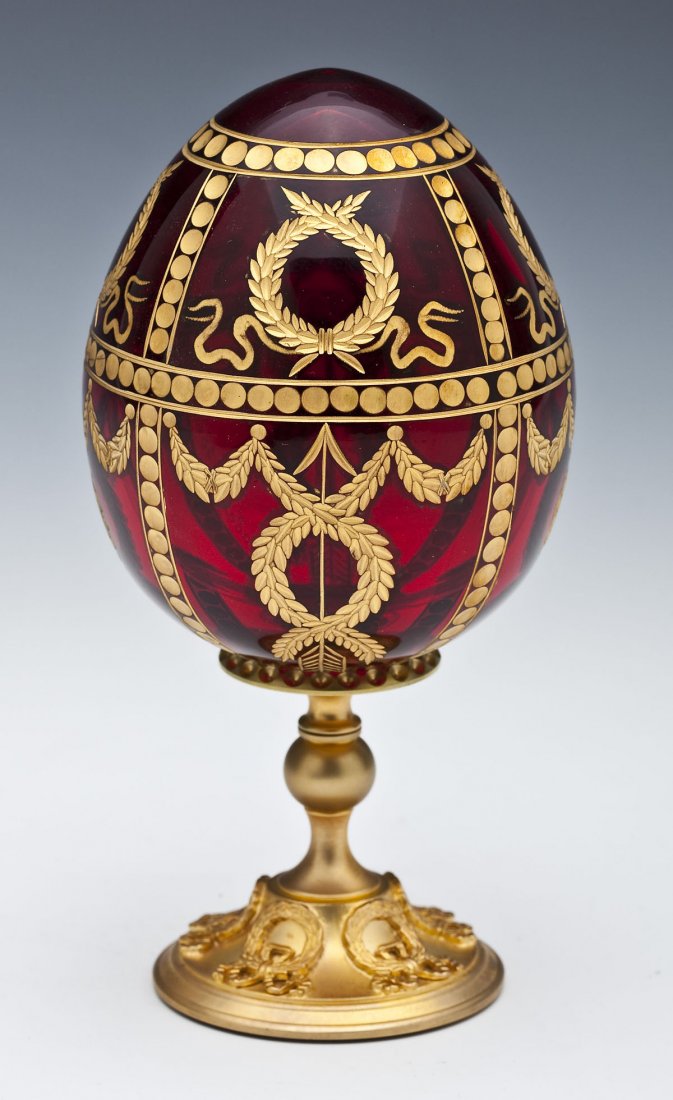 Fabergé Glass Rosebud Egg on Stand: DESCRIPTION: A Fabergé Rosebud glass egg on stand. Ruby glass with gilded engraved wreath and swag decoration overall. On gilded attached pedestal base marked "Fabergé." Egg inscribed "Fabergé 0820