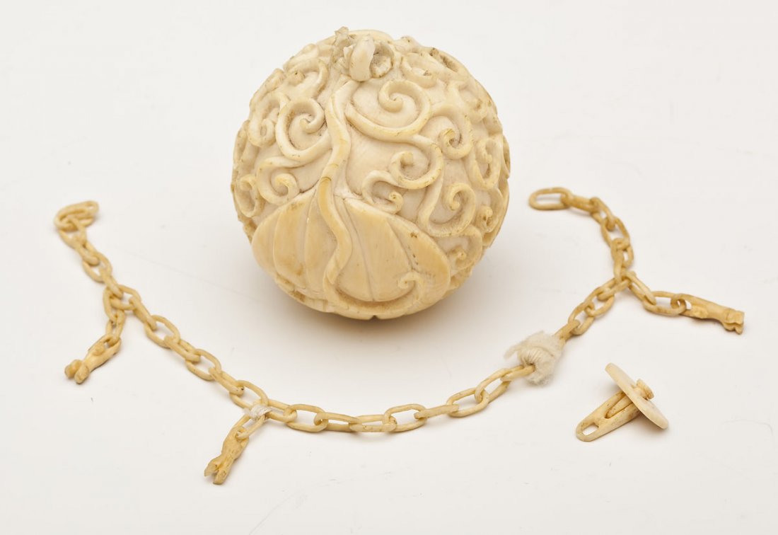 Carved Ivory Mystery Ball: DESCRIPTION: Carved ivory mystery ball with a screw on top and chain with three figural charms. Carved lotus leaf and scroll design. Hollow interior. MEASUREMENTS: Ball 2" diameter. Chain 7" long. CON