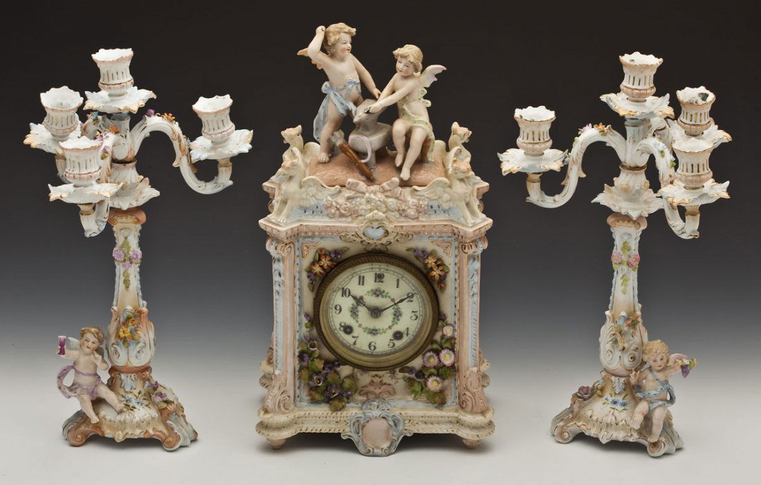 Rudolstadt & New Haven Clock Co. Garniture Set: DESCRIPTION: Rudolstadt porcelain garniture set. Mantle clock with scrolling and floral decoration in relief and griffin corners surmounted by two putti. Eight day time and strike New Haven movement w