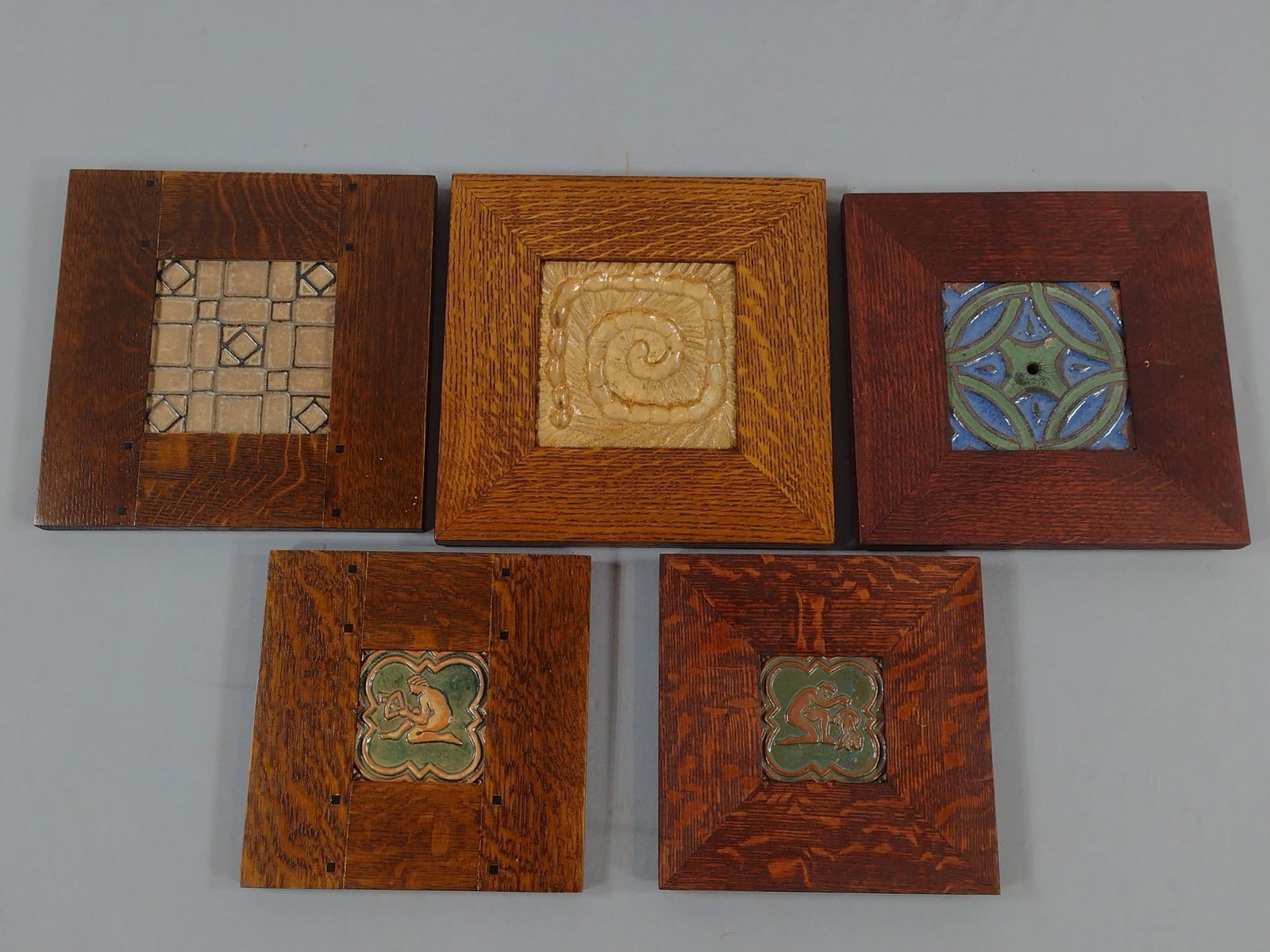 5 Framed Ceramic Tiles: NOT ELIGIBLE FOR IN-HOUSE SHIPPING. Includes one red clay signed Marblehead pottery tile with hand-carved snail/rope type decoration, one red clay tile with Grueby-type glaze and one factory imperfect