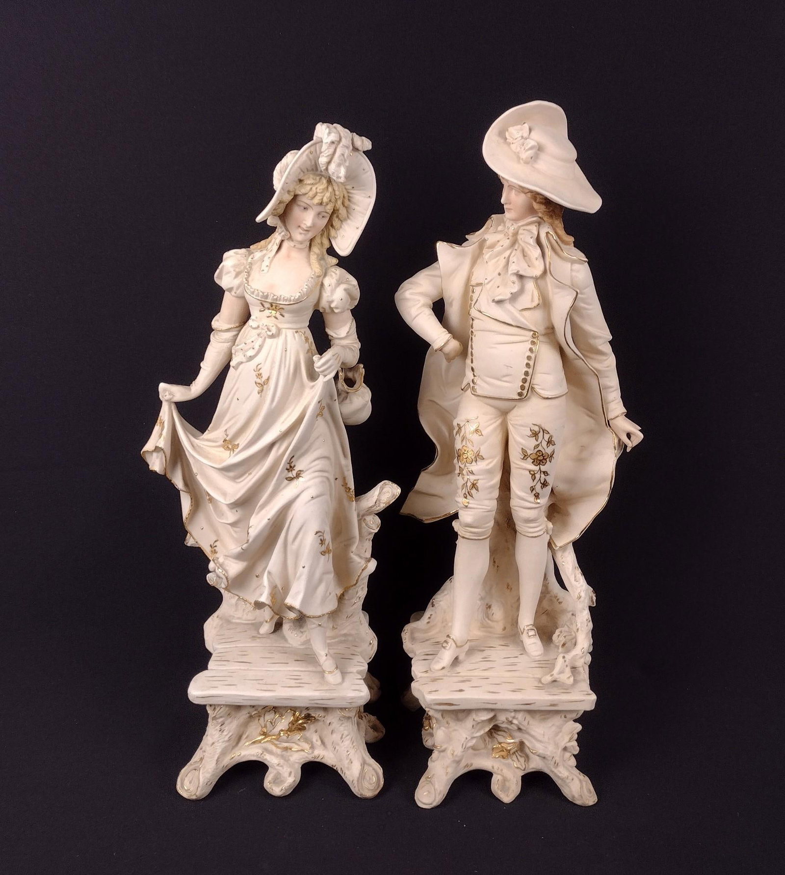 L. Straus & Sons, Rudolstadt, Germany Bisque Figurines: Both marked on bottom. 5" to 5-1/2" wide x 17-1/2" to 18-1/4" high. Tinted with gilt highlights, Gentleman and Lady in 18th century costume. Crack in female's arm.