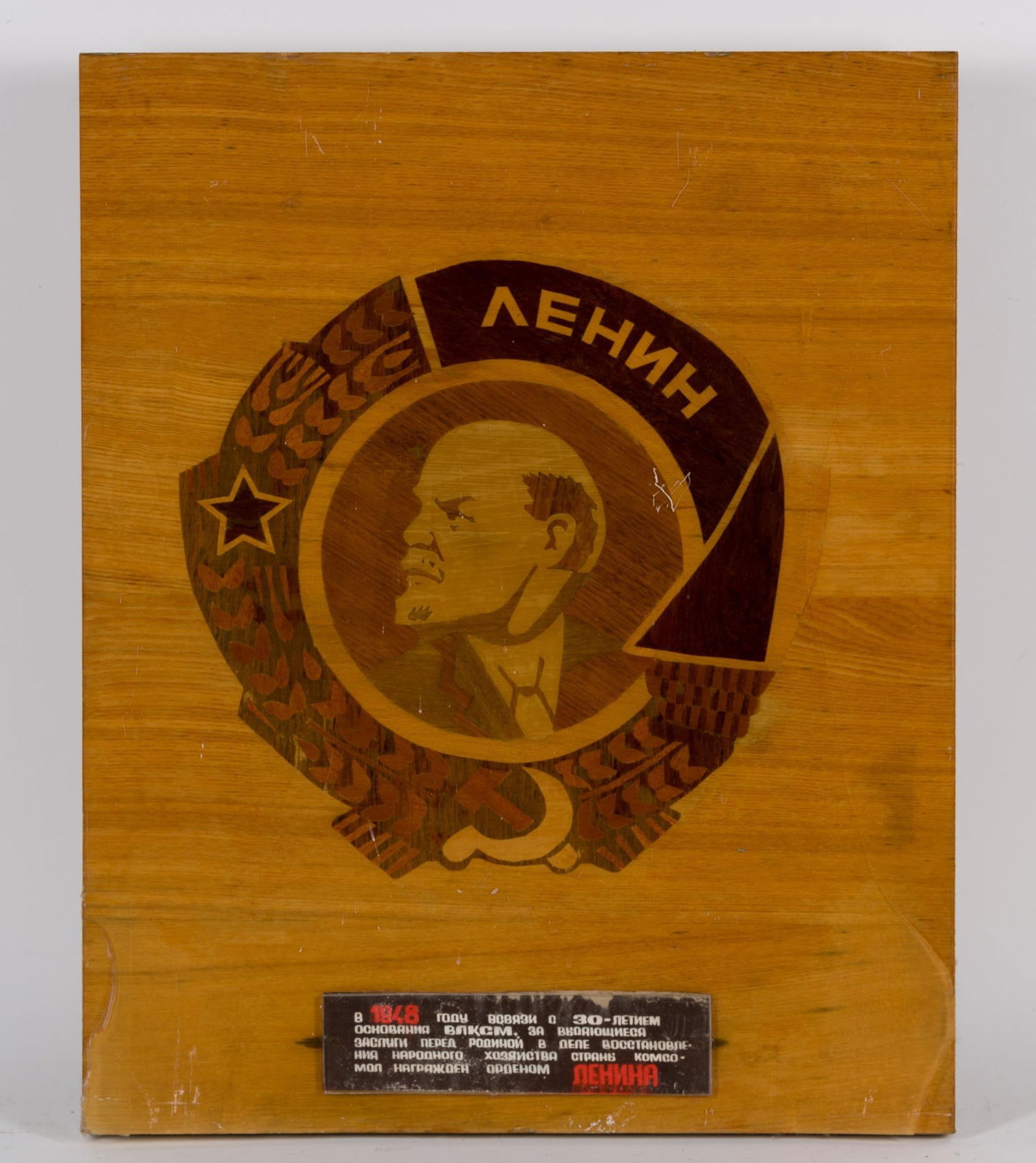 Marquetry Order Of Lenin Wood Plaque: NOT ELIGIBLE FOR IN-HOUSE SHIPPING. DESCRIPTION: Has Russian 1948 caption. MEASUREMENT: 21 3/4" X 17 1/2". CONDITION:Sheet plastic protective cover broken with losses. Wood has minor staining