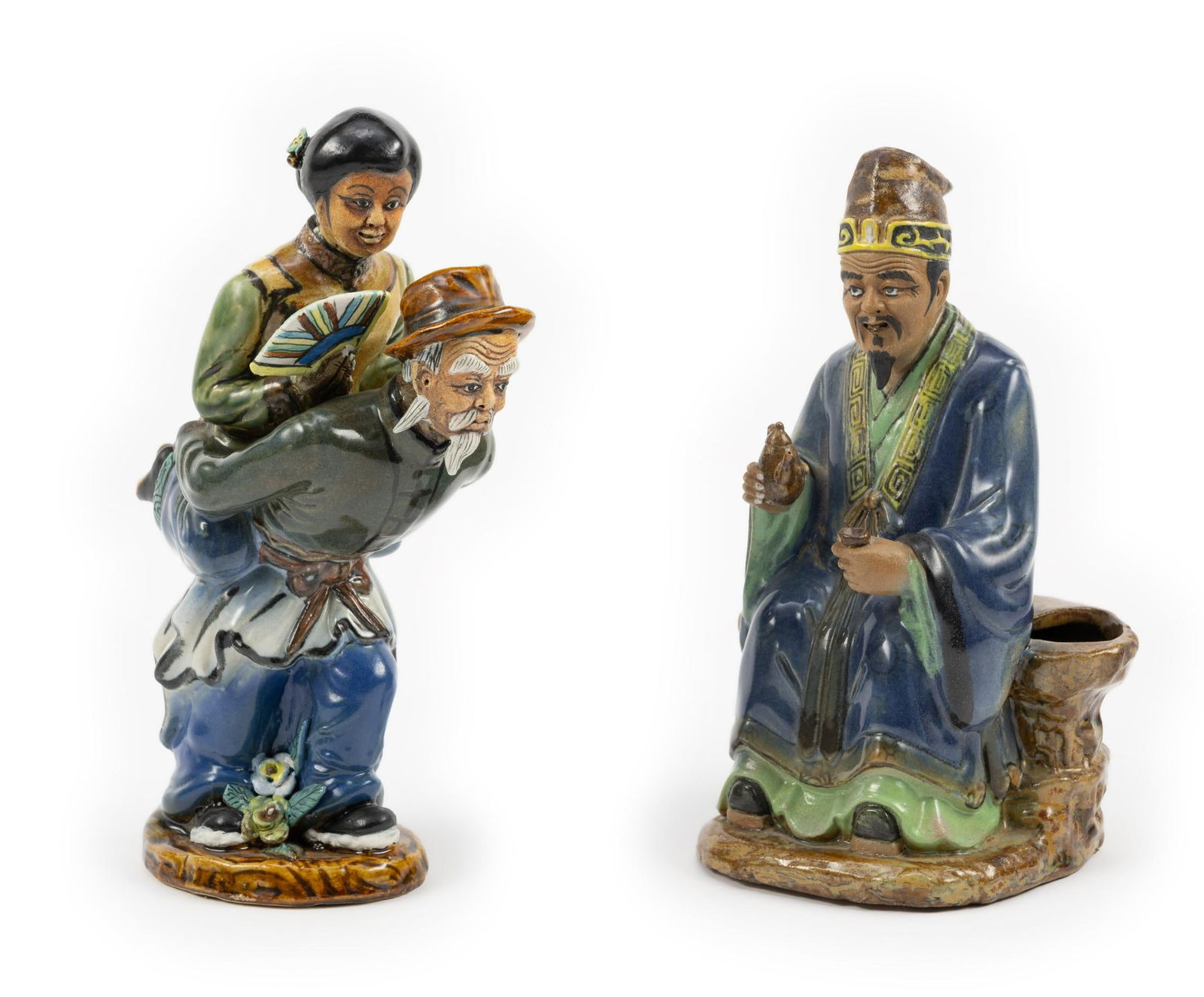 2 Chinese Mudmen Figurines: DESCRIPTION: Includes old man sitting down pouring a cup of tea and man with a woman holding a fan on his back. MEASUREMENT: 3" to 5" wide x 9" to 9-1/4" high. CONDITION: Female's head has been reatta