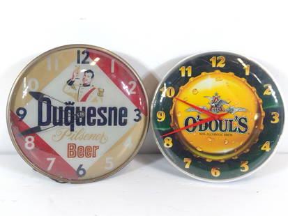2 Beer Advertising Clocks incl Duquesne: NOT ELIGIBLE FOR IN-HOUSE SHIPPING. Untested. 14" to 15" diameter. Some wear and / or rusting consistent with age and use. PROVENANCE: From the Collection of Robert L. Hassenplug—a proud veteran and