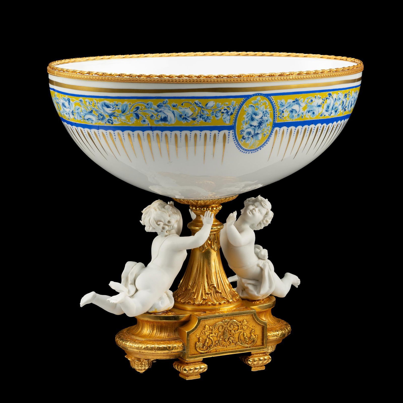Large Porcelain Cherub Decorative Compote w/ Bronze: NOT ELIGIBLE FOR IN-HOUSE SHIPPING. DESCRIPTION: Marked Decrotiche (Tiche Porcellane d'Arte). Centerpiece compote with oval bowl having a blue floral border and gilt metal rim on a bisque porcelain ch