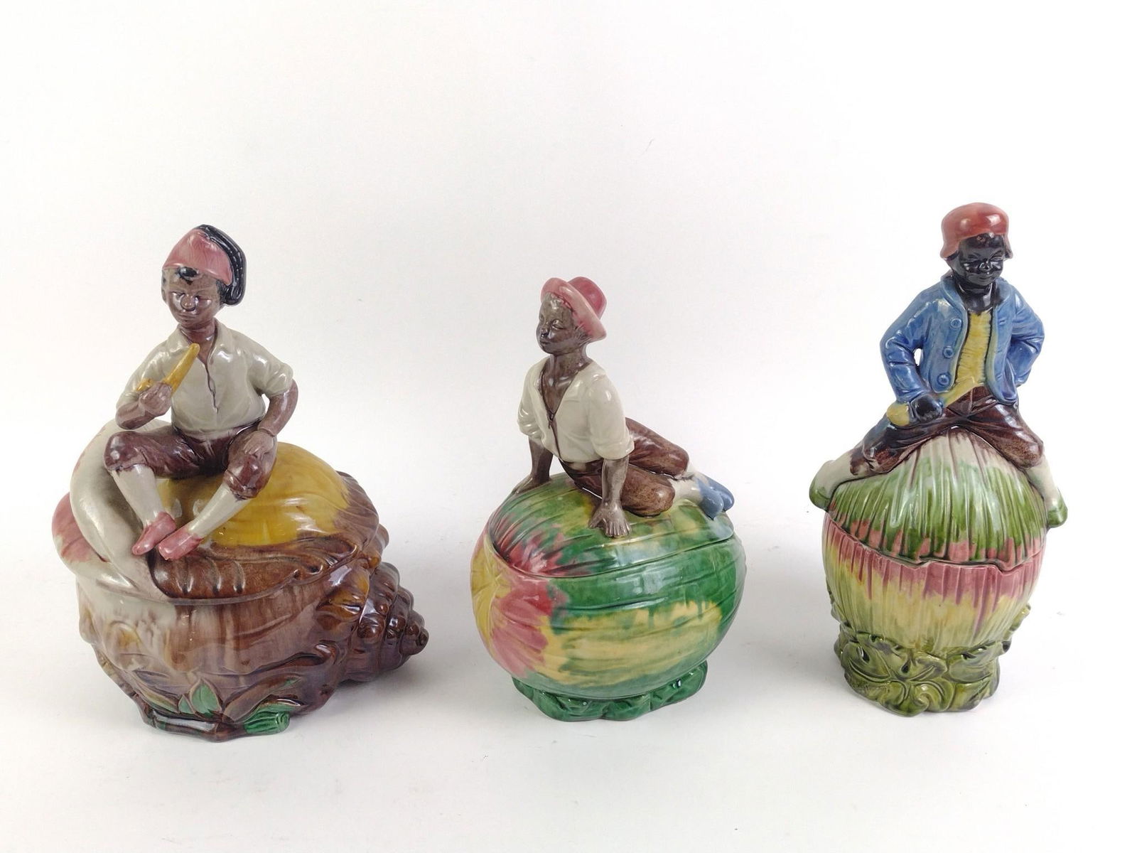 3 Porcelain Black Americana Jars: 3 figural jars of people sitting on top of plants. Overall good condition with normal wear and tear associated with age. From 10" to 11" tall and 5-1/4" to 8" wide.