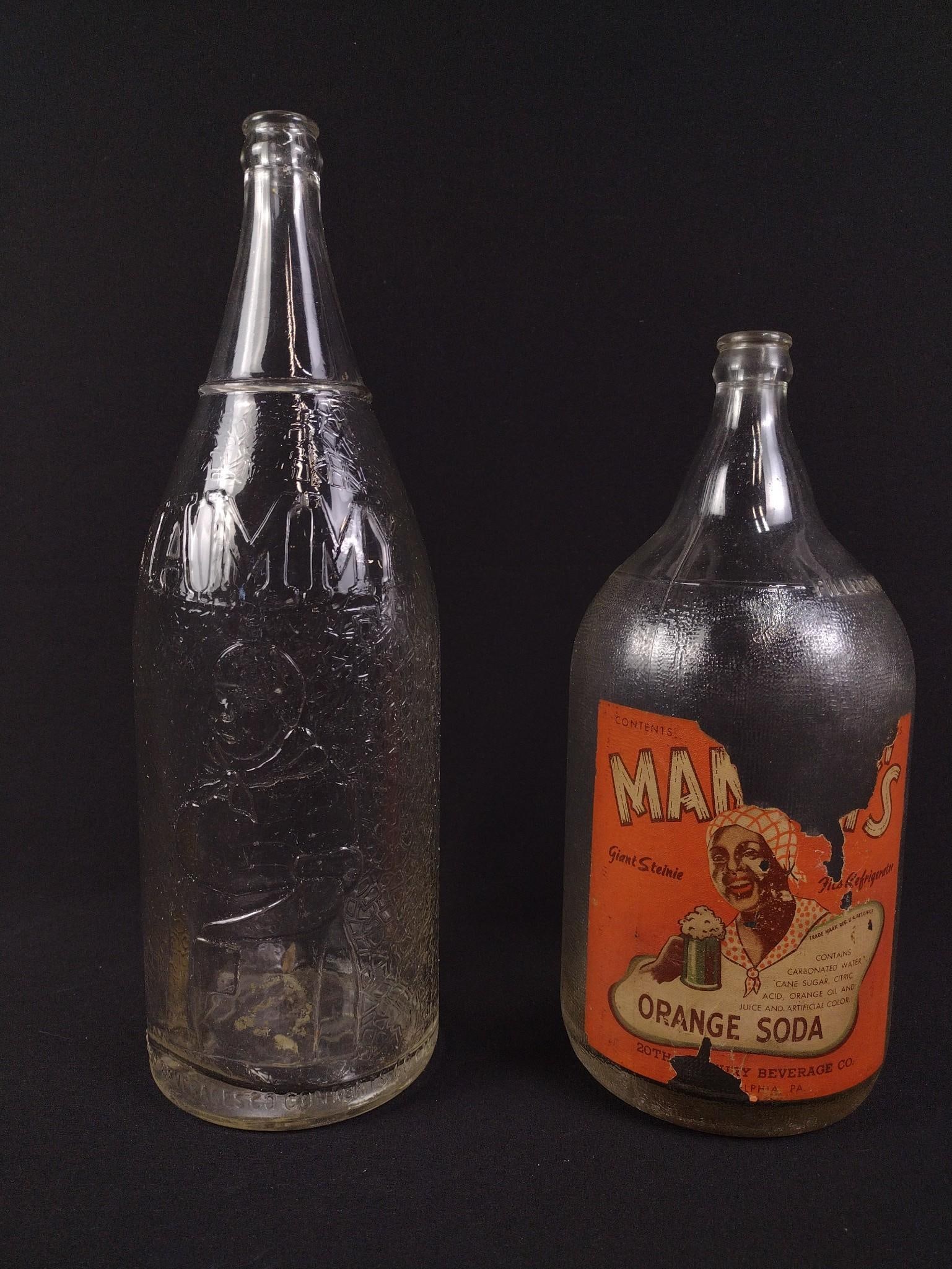 2 Large Black Americana Mammy Glass Bottles: Includes Mammy's Orange Soda bottle with partial label and clear bottle just titled "Mammy." Overall good condition, except Mammy's Orange Soda bottle has a ripped label. From 11" to 13-1/2" tall and 