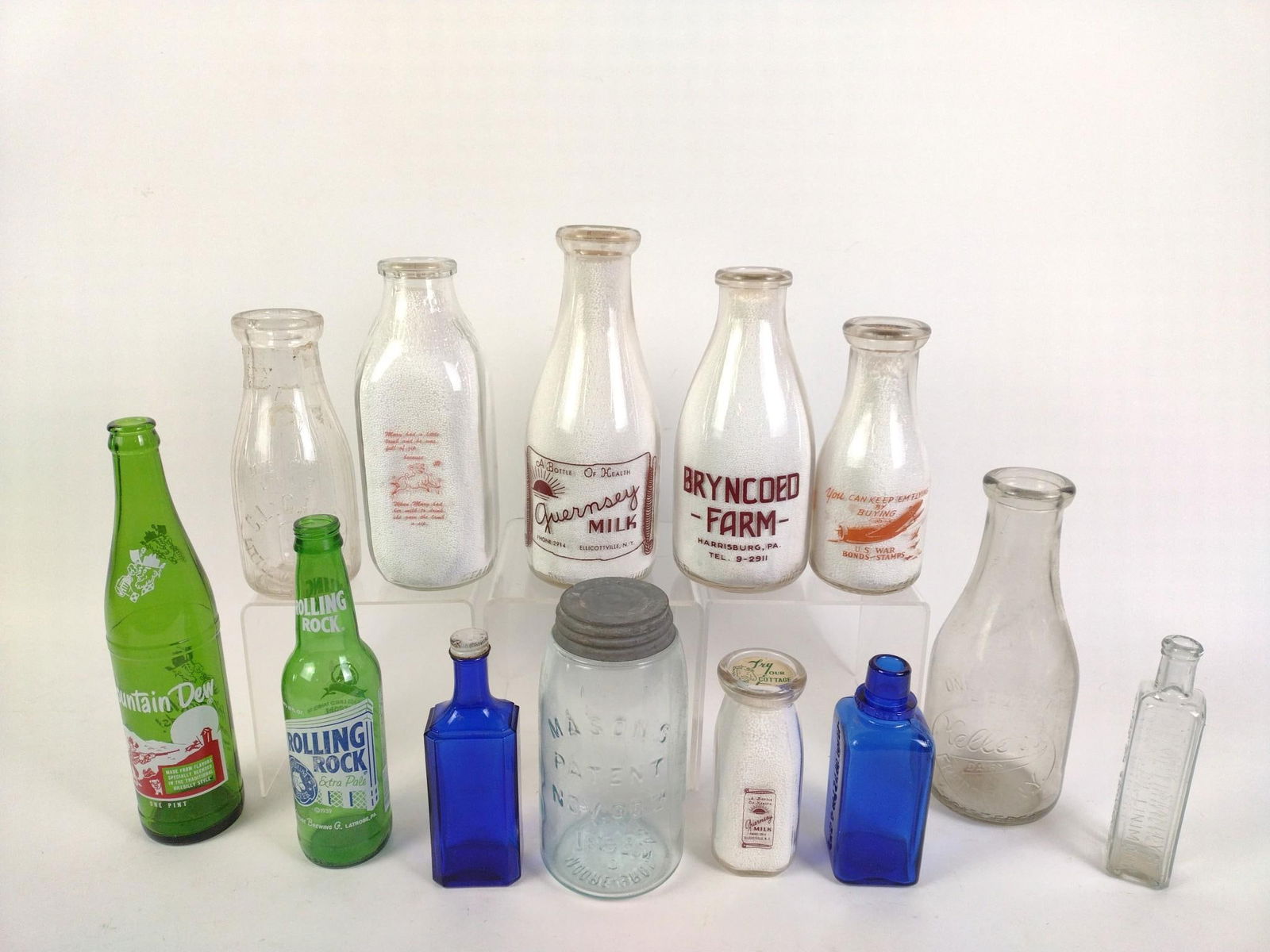 13 Vintage Glass Bottles: Includes 5 milk bottles, one from Bryncoed Farm, Harrisburg, PA, all with advertising lids and filled with white beads. Also includes 1 Mountain Dew bottle, 1 Rolling Rock beer bottle (Latrobe Brewing