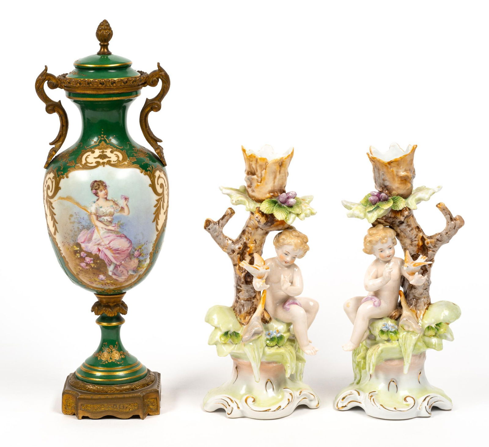 Porcelain Candlesticks and Urn: Includes pair of cherub candlesticks and porcelain mounted urn. 4" to 4-1/4" wide x 8" to 12" high. Large crack and repair to back of urn.