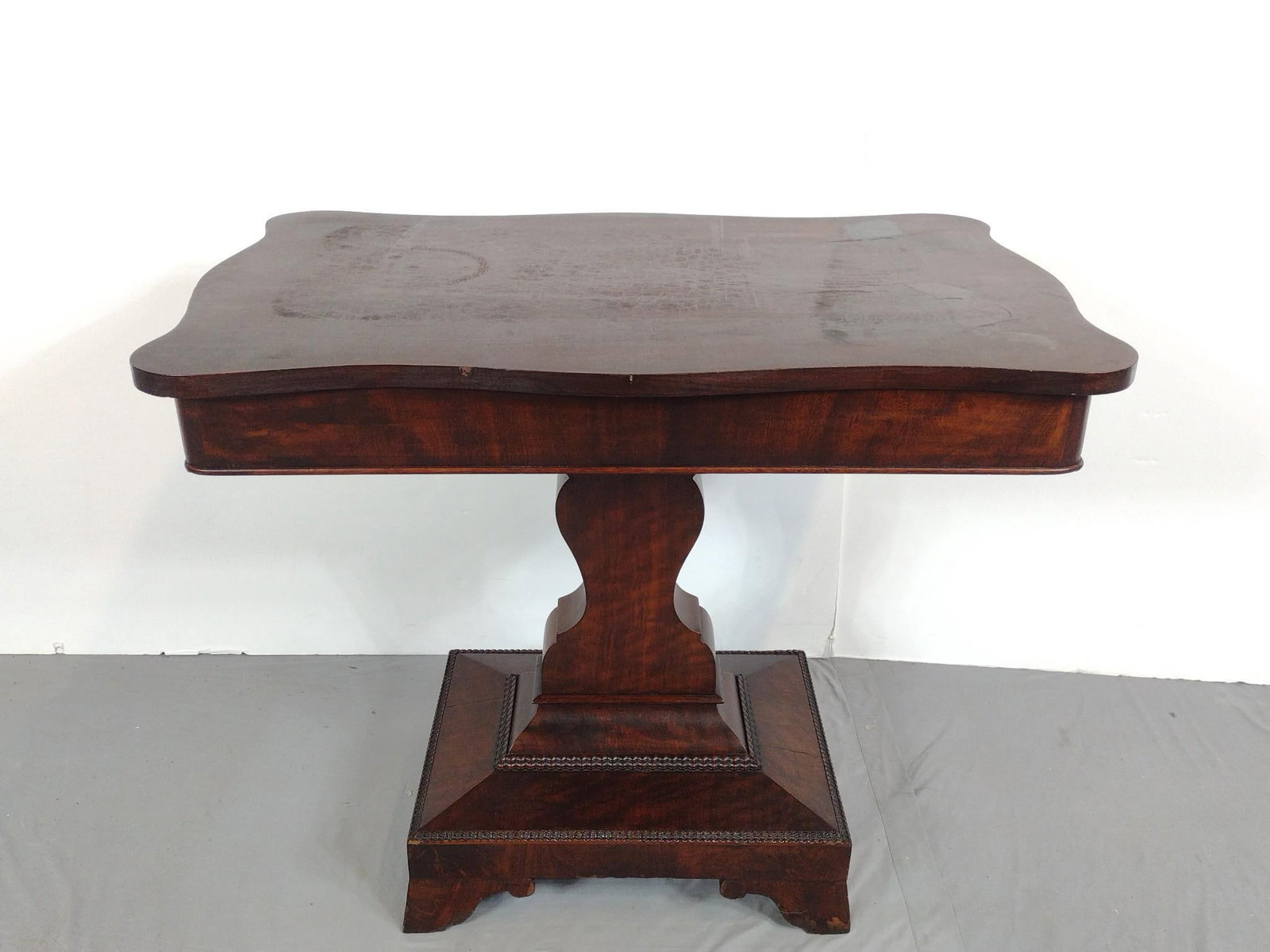 Antique American Empire Pedestal Center Game Table: NOT ELIGIBLE FOR IN-HOUSE SHIPPING: See Terms for Shipping Options. 33-1/2" wide X 22" deep X 28" high. Top has some scratches and areas of discoloring. Has some veneer losses at base.