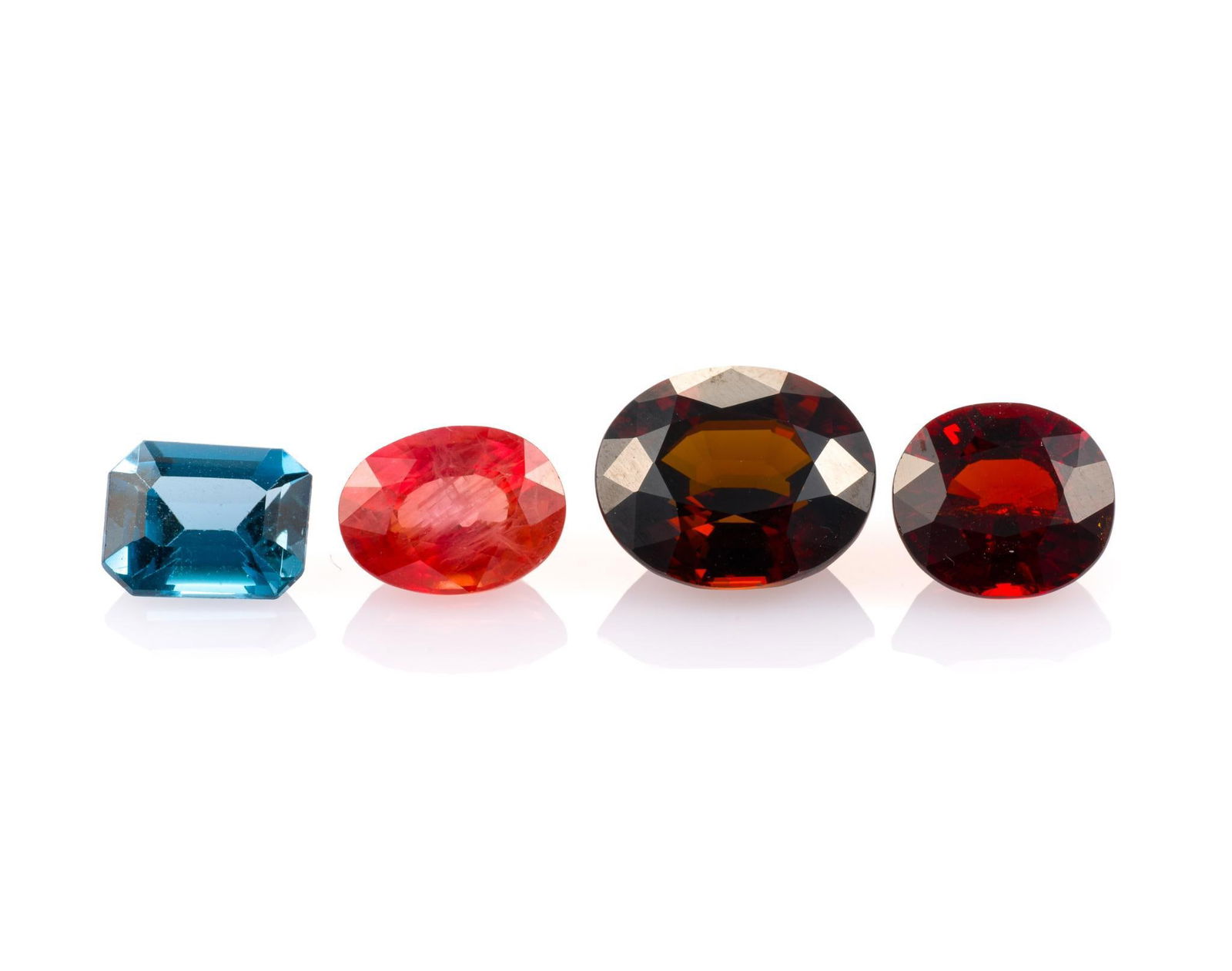 4 Unmounted Gemstones: Includes (1) Sapphire, oval, 2.45 carats, VS, heated; (2) Topaz, emerald cut, 1.898 carat, VVS, irradiated; (3) Spessartite Garnet, oval, 3.22 carat, VVS, natural; and (4) Sphene, oval, 4.63 carats, V