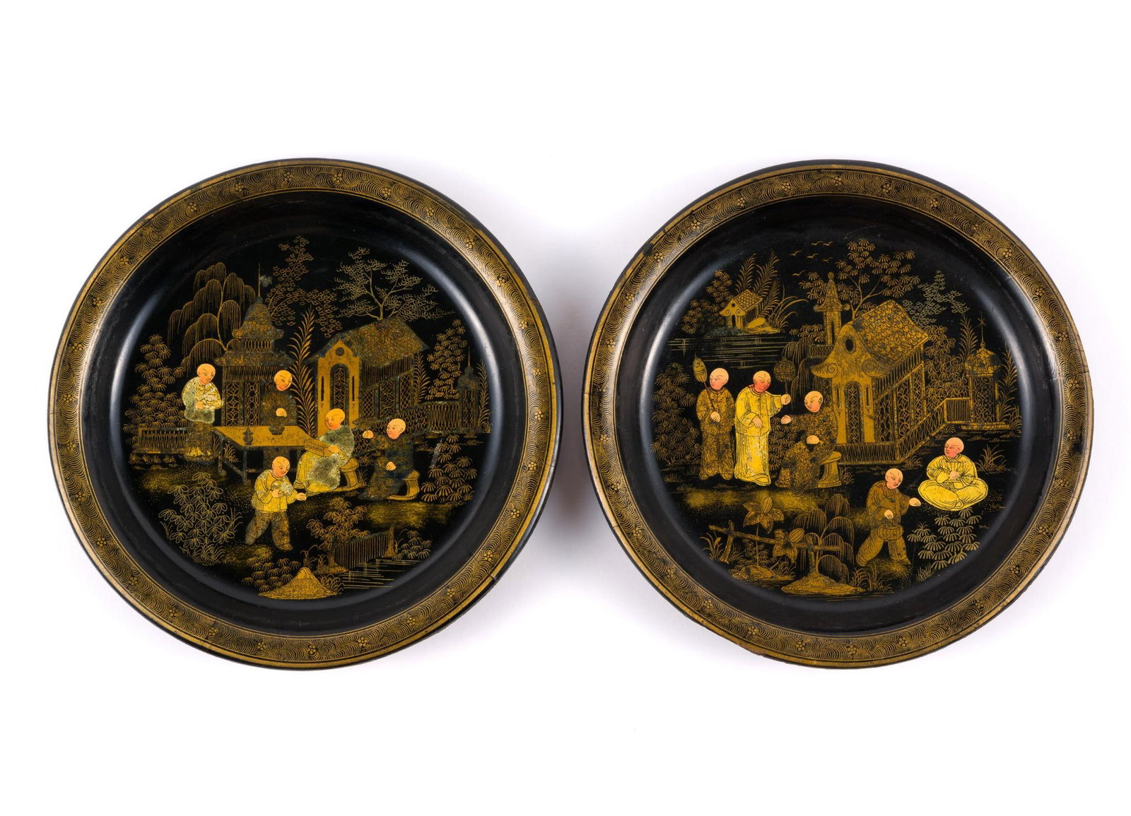 2 Japanese Import Black Lacquer Plates: Both depict a group scene in front of a pagoda and lake. Both 8" diameter. Some losses to the edges of the plates.