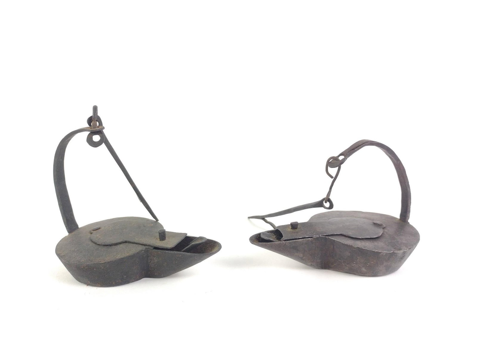 Pair of Antique Iron Betty Lamps: Pair of antique wrought iron Betty lamps with hinged lids and hanging handles. Each measures approximately 5 in. x 5 1/4 in. Condition consistent with age. Betty lamps were simple oil-burning lamps