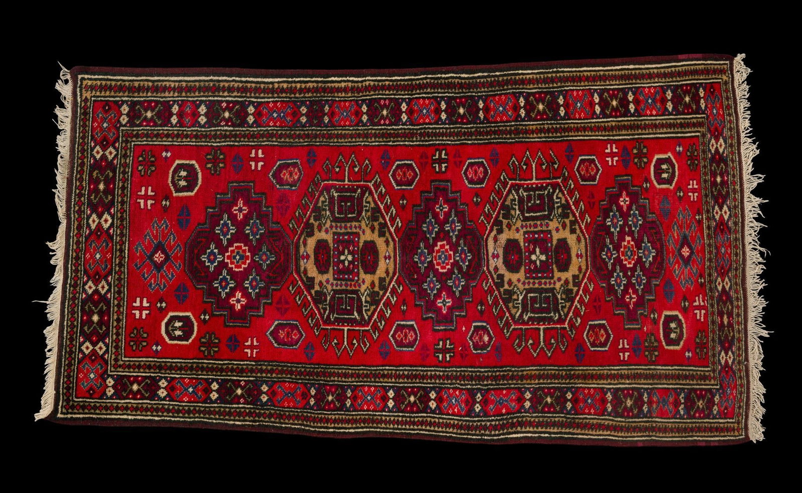 20th Century Bokhara-Style Accent Rug: Hand-knotted wool rug featuring rows of octagonal gul medallions on a red field within multiple geometric borders. Finished with fringe ends. Minor fringe wear and general wear associated with age and