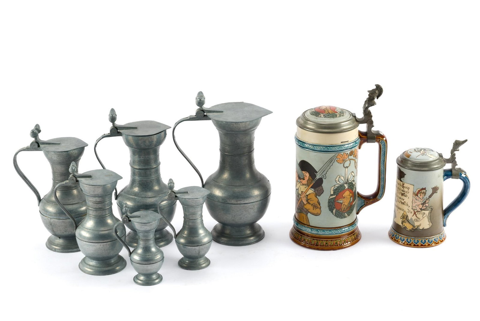 2 Steins and Pewter Jugs Set: Includes 6 pewter jugs/pitchers with an acorn-like finial on top, varying in size. Also, two Mettlach steins (1 1-Liter & 1 3/10-Liter). All in good condition. Smallest measures 5"; largest measures